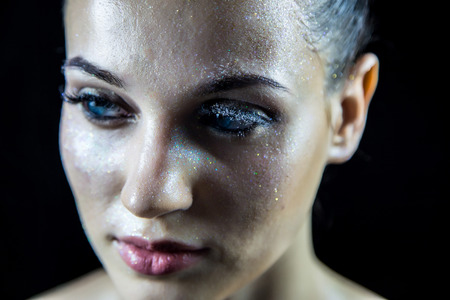 Facial expression and brilliant smile of girl with bright evening make-up, shiny glamor glow cosmetics. The creative makeup of the girl is covered with sparkles dark backgroundの写真素材