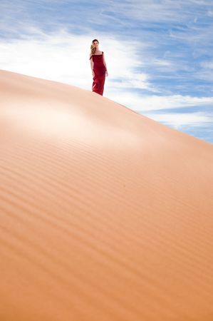 A beautiful woman in red dress walking on pink sand dunesの写真素材