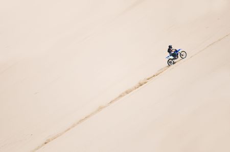 A motorcyclist riding up a sand duneの写真素材