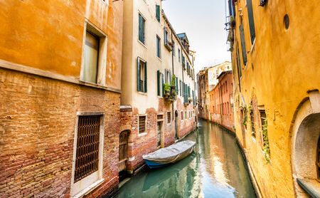 Quiet Yellow Venetian Canal with Boat in Still Water, Venice, Italyの写真素材