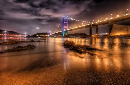 Wide Angle View of Ma Wan Island Suspension Bridge from the Beach at Night with Vibrant Reflections in the Water, Hong Kongの写真素材
