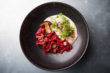Red ravioli with mushrooms served on a black plateの写真素材