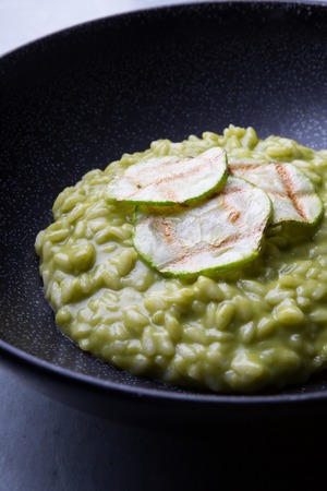 Green risotto with zucchini served in a black bowlの写真素材
