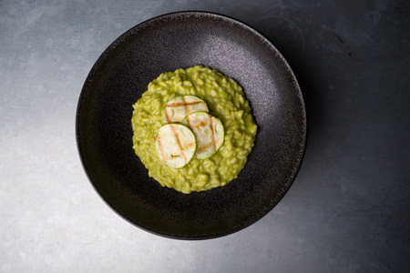 Green risotto with zucchini served in a black bowlの写真素材