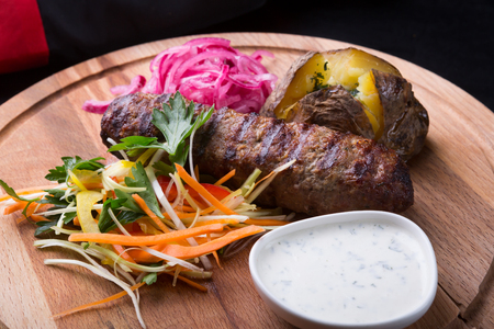 Grilled kebab served with baked potato on wooden boardの写真素材