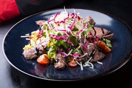 Roastbeef sliced served with vegetables salad on a dark plateの写真素材