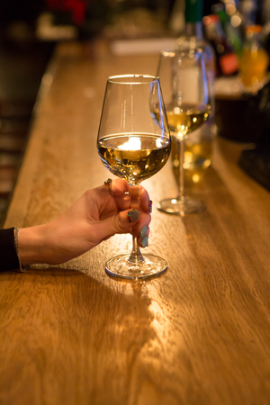 Hand holding glass of white wine ant the bnar counterの写真素材