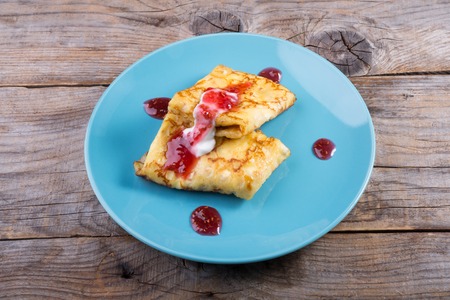 Pancakes served with cream and red jam on a blue plateの写真素材