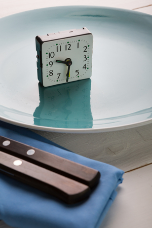 Alarm clock on an empty plate on a tableの写真素材