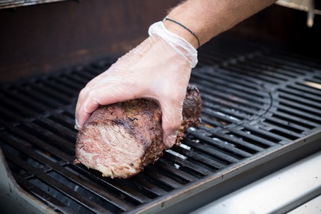 Palm in glove preparing beef on a metal grillの写真素材