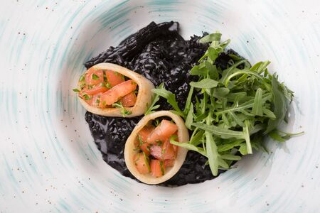 Black seafood risotto served with arugula on a white plateの写真素材