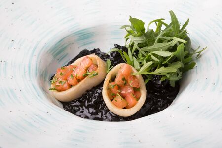 Black seafood risotto served with arugula on a white plateの写真素材