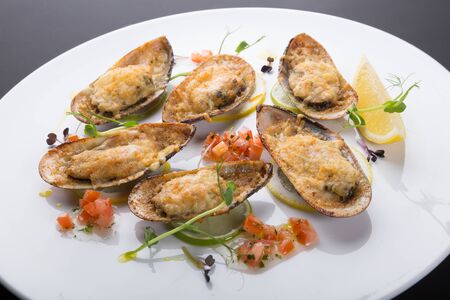 Mussels baked with cheese and served with lemon on a plateの写真素材