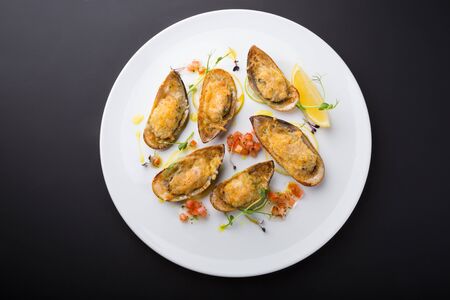 Mussels baked with cheese and served with lemon on a plateの写真素材