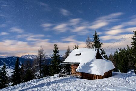 A night view of a little hut with snow on top and a dark blue night sky with stars in Wagrain,...