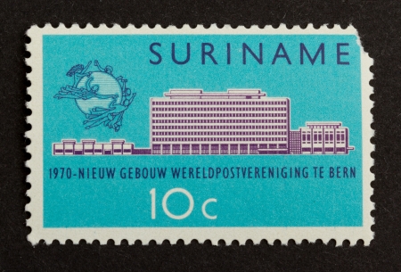 SURINAME - CIRCA 1970: Stamp printed in Suriname shows a a large building, circa 1970のeditorial素材