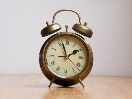Retro alarm clock on a wooden table with a white wallの写真素材