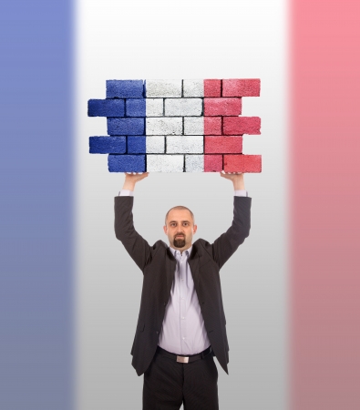 Businessman holding a large piece of a brick wall, flag of France, isolated on national flagの写真素材