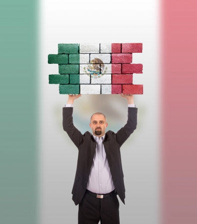 Businessman holding a large piece of a brick wall, flag of Mexico, isolated on national flagの写真素材