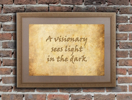 Old wooden frame with written text on an old wall - A visionary sees light in the darkの写真素材