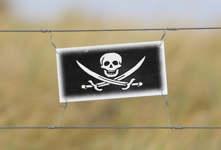 Border fence - Old plastic sign with a flag - Pirateの写真素材