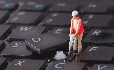 Miniature worker with drill working on a computer keyboardの写真素材