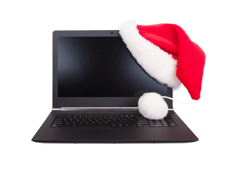 Modern open laptop with red santa claus hat put on lcd corner, isolated on whiteの写真素材