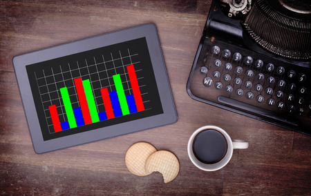 Tablet touch computer gadget on wooden table, graph, vintage look