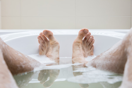 Men's feet in a bright white bathtub, selective focus on toes