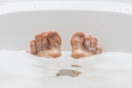 Men's feet in a bright white bathtub, selective focus on toesの写真素材