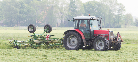 Leeuwarden, the Netherlands - May 26, 2016: Farmer uses tractor to spread hay on a field in Friesland, the Netherlands on May 26, 2016.のeditorial素材