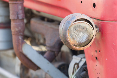 Old tractor face, red, rusty an dented, selective focus on it's lightの写真素材