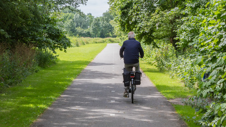 Unrecognisable old man riding a bike on asphalt road