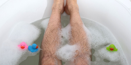 Men's feet in a bright white bathtub, selective focus on toesの写真素材