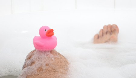 Men's feet in a bright white bathtub, selective focus on toesの写真素材