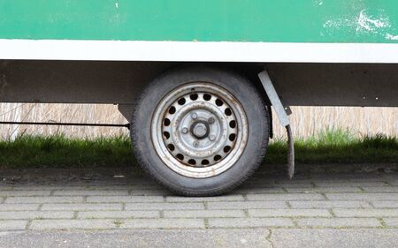 Wheel of an old green wooden trailer on wheels stands at the side of the road, the Netherlands