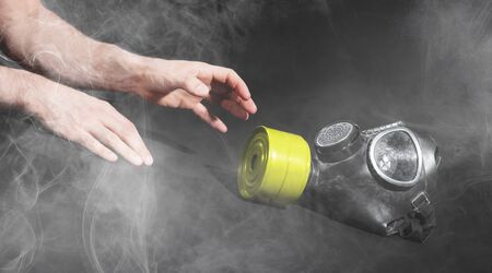 Man in room filled with smoke, trying to reach for vintage gasmask - Isolated on black - Yellow...