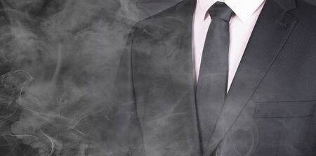 Man in a black suit and black tie, standing in smoke, close-upの写真素材