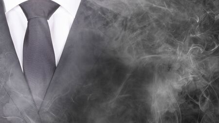 Man in a black suit and black tie, standing in smoke, close-upの写真素材
