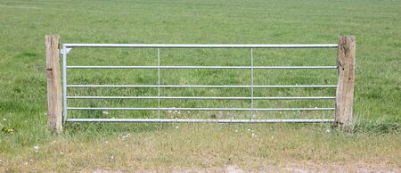 Metal fence and farm gate leading into grassy field, the Netherlandsの写真素材