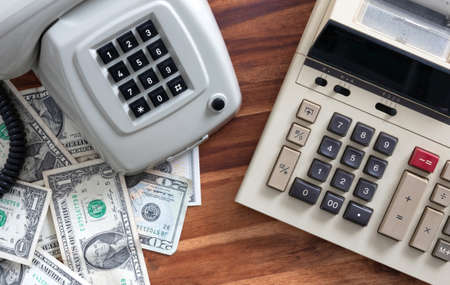 Old fashioned calculator, telephone and dollars on deskの写真素材