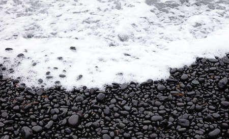 Waves crashing on a black pebble beach on Iceland, cloudy summerの写真素材