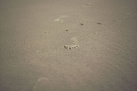 detail of a foot prints on a sandy beach next to waves