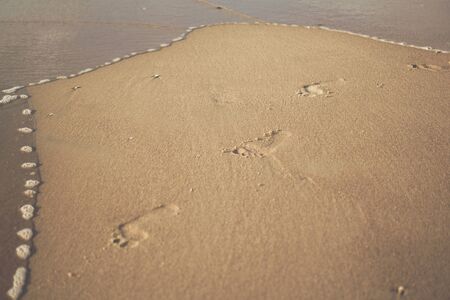 detail of a foot prints on a sandy beach next to wavesの写真素材