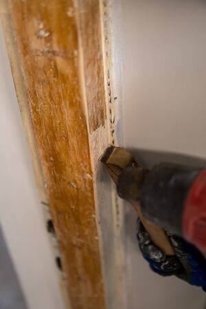 Detail of removing old white paint from door frame with heat gun and scraper
