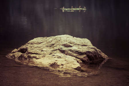 single rock in a shallow water of a lake