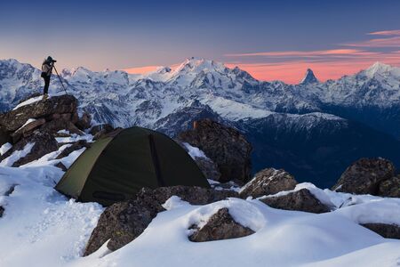 Winter camp, night, green tent in the snow. Night shot, long exposure, sleeping in the snow outside. Alps mountains landscape panoramic view. Winter day in Switzerland, Europe.の写真素材