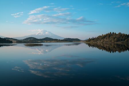 Reflection of snow capped Mount Shasta in a clear water in a lake at sunrise in California State, USA. Mount Shasta is a volcano in the southern end of the Cascade Range in Siskiyou Countyの写真素材