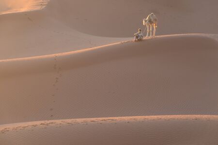 Bedouin and camel on the desert through the desert Beautiful sunset with caravan on Sahara, Morocco Desert with camel and nomads Silhouette nomad man with dramatic sky Picturesque background nature conceptの写真素材