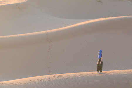 A woman walking in the sand dunes of the Sahara desert, Moroccoの写真素材